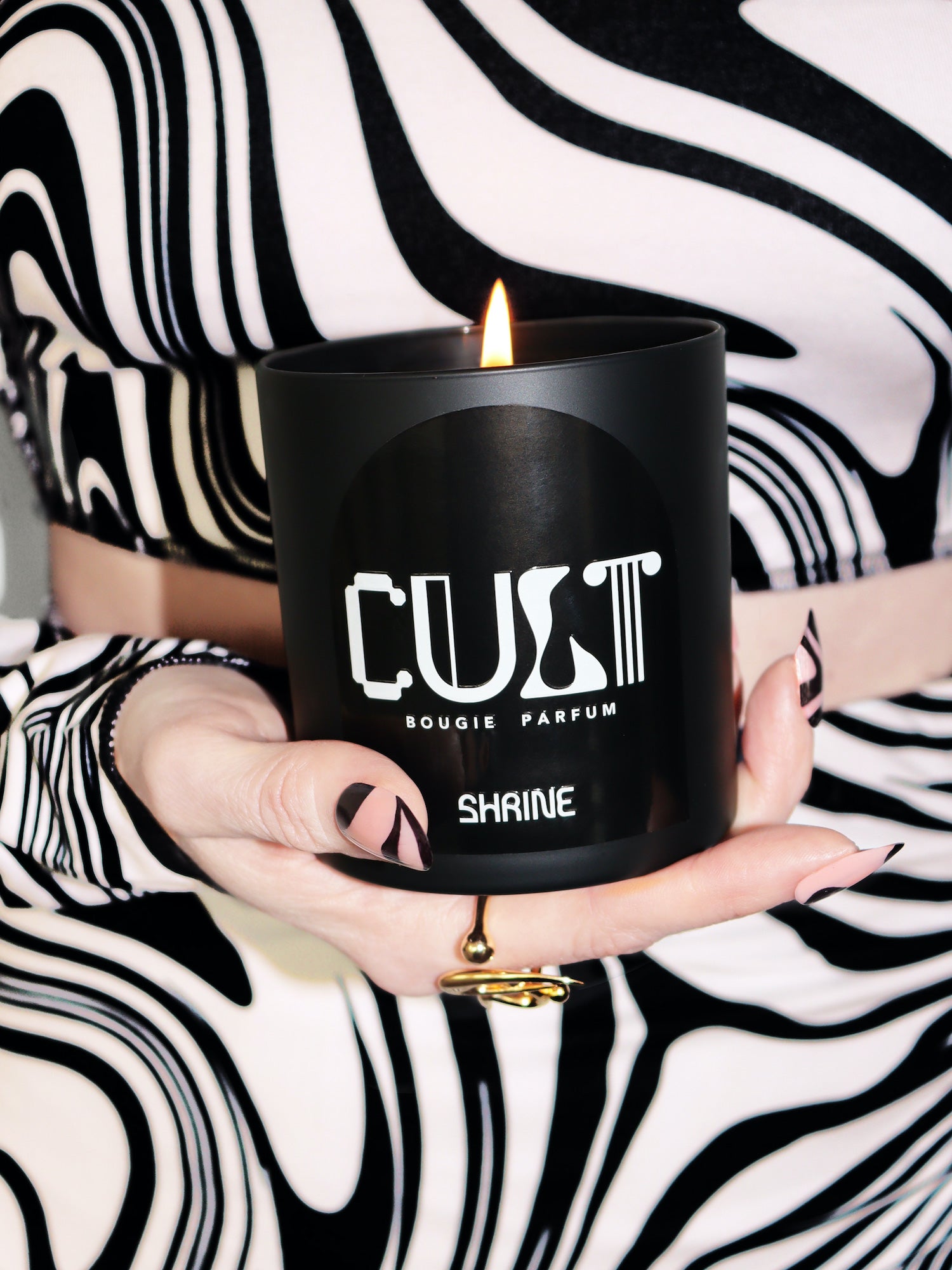shrine shop shrine black monochromatic cult scented candle with white text design in a hand with wavy nails and black and white wavy skirt and top