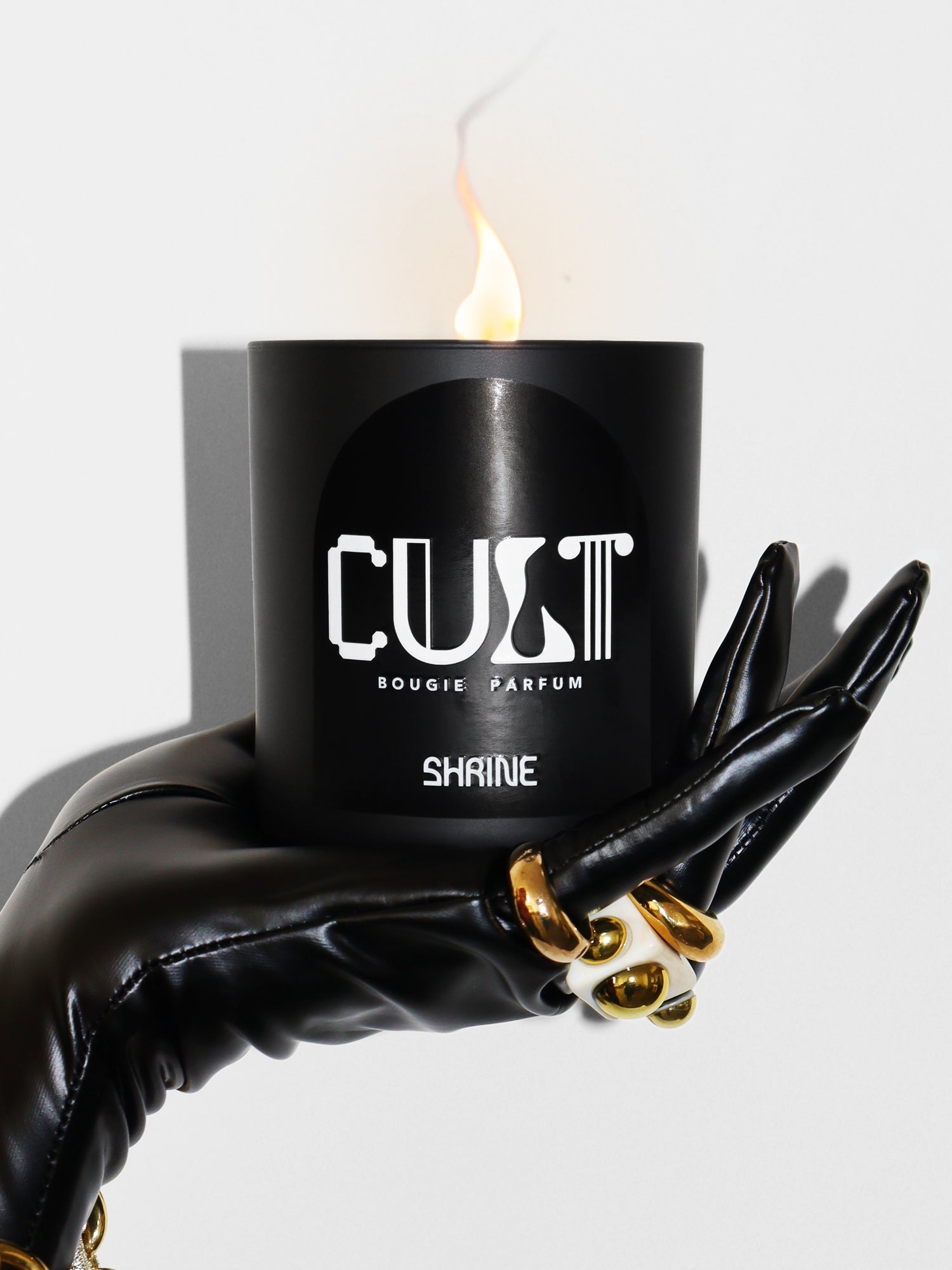 shrine shop shrine cult monochromatic black candle with white text design  in a black patent leather gloved hand with gold rings and gold bracelet shop shrine